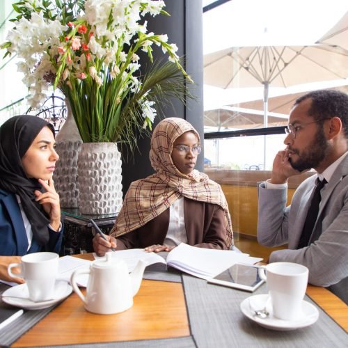 Multiethnic business partners working on agreement Multiethnic business partners working on agreement in cafe. Businessman and Muslim businesswomen sitting in coffee shop, calling on phone and signing documents. Partnership concept