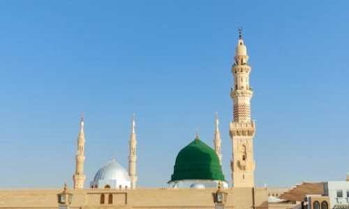 pexels-photo-18360295-18360295 Scenic view of the Prophet's Mosque in Medina, showcasing its iconic minarets and dome under a clear blue sky.
